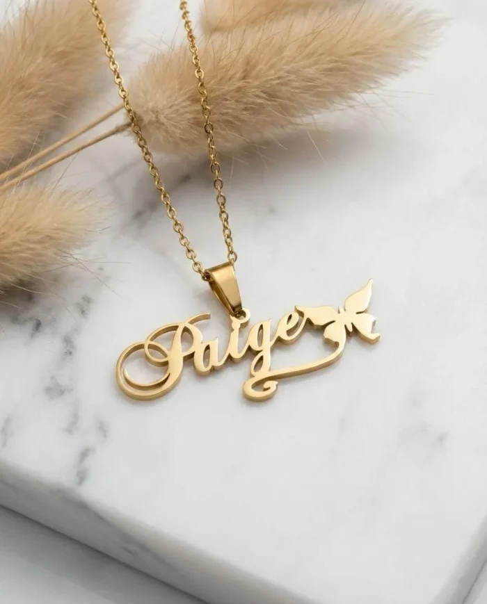 Dainty 18K gold plated stainless steel custom name necklace with the name Paige on it and a butterfly, resting on white marble.